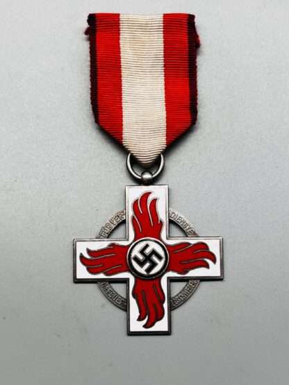 A WW2 German Fire Brigade Honour Cross 2nd Class Medal, constructed in silvered bronze with white and red enamel.   The medal depicts a Geneva-style cross in white enamel with sylised red enamel flames with a mobile swastika in the centre in black enamel, with black, red, and white ribbon.
