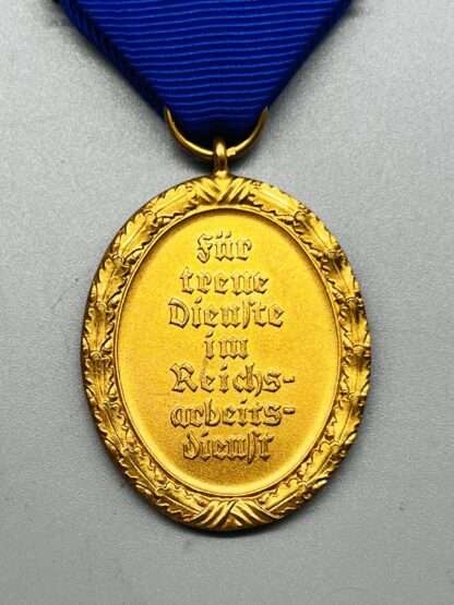 A WW2 German RAD Long Service Medal 1st Class 25 Years constructed in bronze with gilt finish with blue ribbon, oval shaped. The reverse of the medal depicts has the inscription "FÜR TREUE DIENSTE IM REICHSARBEITSDIENST” (FOR FAITHFUL SERVICE IN THE REICH LABOUR SERVICE).