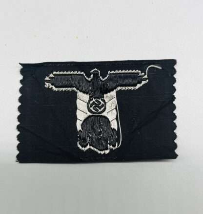 The reverse image of a Waffen-SS Panzer M43 Trapezoid BeVo flat wire construction in silver thread on black backing which depicts a SS National Eagle with a skull below.