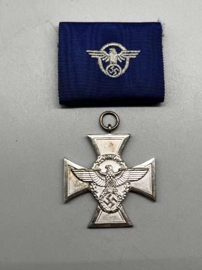 A WW2 German Police Long Service Medal 18 Years, constructed in silvered tombac with a period blue ribbon embroidered with police insignia with police emblem embossed in the centre.