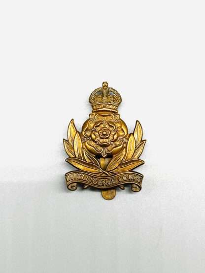 A Intelligence Corps Cap Badge, constructed in brass. The badge depicts a rose in the centre surmounted by an imperial King's crown, between twin sprays of laurel with a scroll below bearing the inscription Intelligence Corps.