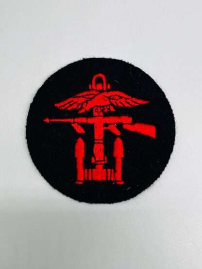 A British Combined Operations Badge embroidered with red thread on dark blue wool backing circular shaped.