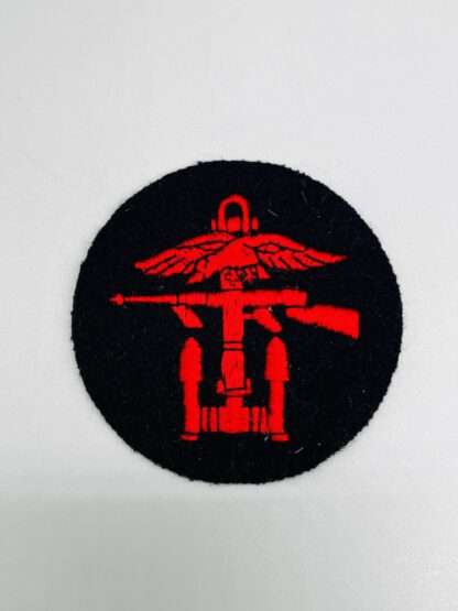 A British Combined Operations Badge embroidered with red thread on dark blue wool backing circular shaped.