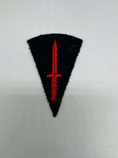 A post war Commando badge depicts a red commando dagger, pointed upwards on a black inverted black triangle with a rounded top.