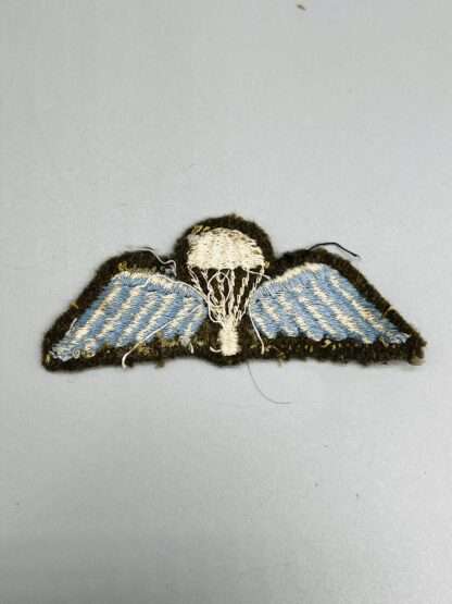 A reverse image of British WW2 Paratrooper Jump Wings embroidered in white and blue thread on khaki green backing.