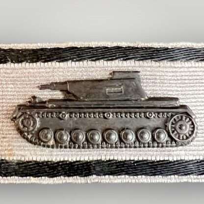 close image of a WW2 German tank destruction badge in silver, contructed in blackened metal on silver aluminium bullion backing with two black strips of black thread above and below.