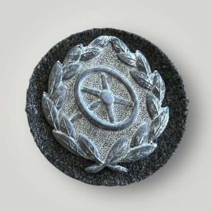A Heer (Army) driver's proficiency badge in silver, die-stamped construction with silver finish mounted on green wool backing.