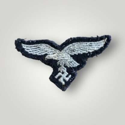 A reverse image of a Luftwaffe M43 cap eagle, machine embroidered in white thread on blue wool backing.