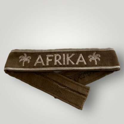 An original WW2 German Afrika Korp Officer's cuff title machine embroidered constructed in camel hair khaki-colored with the inscription "AFRIKA" in silver thread flanked by palm trees.