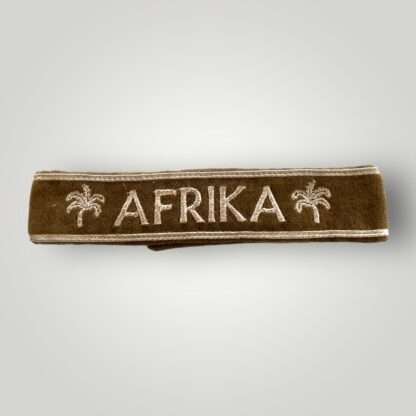 An original WW2 German Afrika Korp Officer's cuff title machine embroidered constructed in camel hair khaki-colored with the inscription "AFRIKA" in silver thread flanked by palm trees.