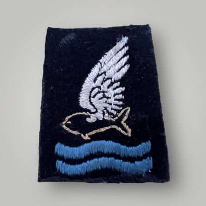 A scarce British WW2 RAF Goldfish Club Badge hand embroidered on black wool and depicts a white winged goldfish flying over two waves.