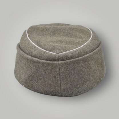 An original M43 Schutzmannschaft Officer’s Field Cap, constructed in grey field grey wool with aluminium wire piping running around the top of the outer edge of the crown, with two  pebbled and grey-painted zink buttons.