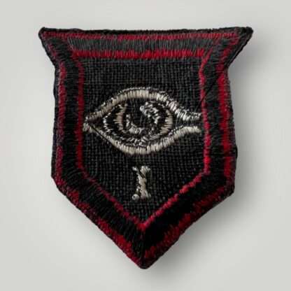 Reverse image of an British WW2 1st Armoured Guards Division formation badge, machine embroidered in dark blue shield with red outer border within which an eye motif above the figure I
