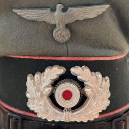 Close up image of an original WW2 German (Heer) Panzer EM/NCO's visor cap, constructed in grey-green doeskin with three bands of pink pipping for Panzer units and dark green woolen band for Army/Heer with black leather chin strap.