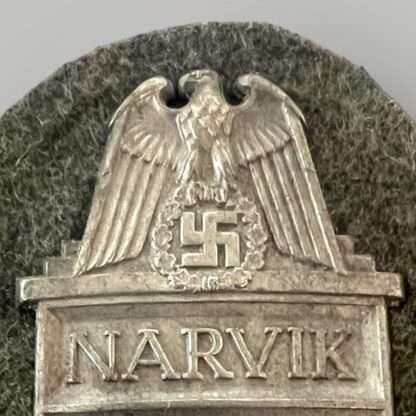 A close up image of a scarce Heer Narvik campaign shield by Deumer, constructed in zink on field grey woollen backing.