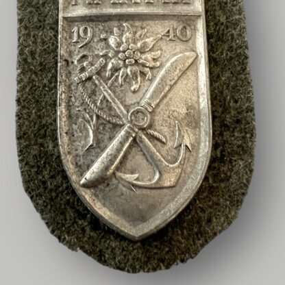 A close up image of a scarce Heer Narvik campaign shield by Deumer, constructed in zink on field grey woollen backing.