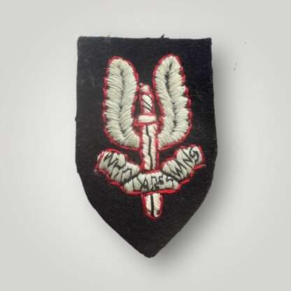 A genuine Special Air Service beret badge for other ranks, hand-embroidered in Oxford blue thread outlined in red thread on a black padded shield.