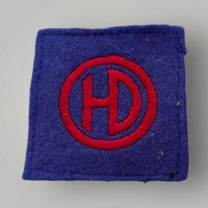 An original British WW2 51st Highland Division formation badge, machine embroiderd depicting the letters HD conjoined in red within a red circle on a blue woollen backing.