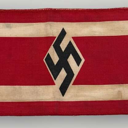 A Hitler Youth Student Bund Armband. The armband is constructed in red cotton with two white stripes along the edges. In the middle, there is a black swastika inside a white diamond, which is a typical symbol of the Hitler Youth