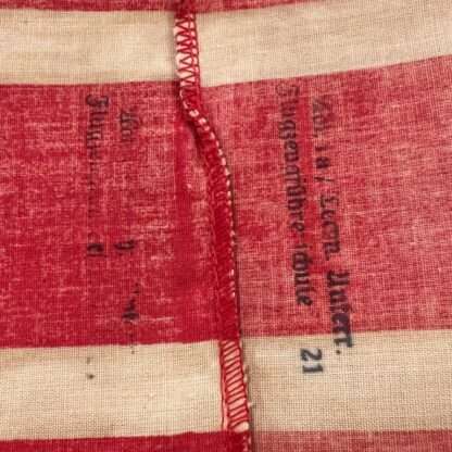 Reverse side of a Hitler Youth Student Bund Armband. The armband is constructed in red cotton with two white stripes along the edges. In the middle, there is a black swastika inside a white diamond, which is a typical symbol of the Hitler Youth.