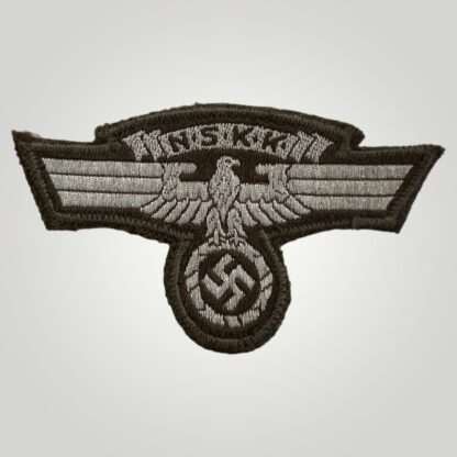 An NSKK sleeve eagle, machine embroidered flat wire bevo construction in silver thread on brown backing. The obverse of the insignia depicts a longed winged eagle used by National Socialist Motor Corp with a scroll above with the organisations initials.