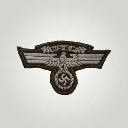 An NSKK sleeve eagle, machine embroidered flat wire bevo construction in silver thread on brown backing. The obverse of the insignia depicts a longed winged eagle used by National Socialist Motor Corp with a scroll above with the organisations initials.