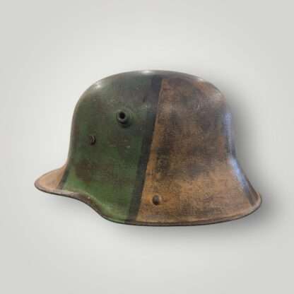 A German M16 steel camouflage WW1 helmet. The exterior of the helmet has been hand painted in tan ochre, green, and black paint.