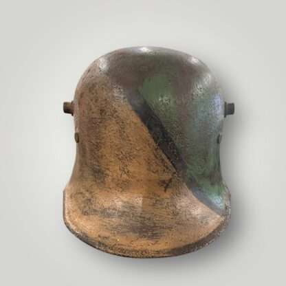 A front view of a German M16 steel camouflage WW1 helmet. The exterior of the helmet has been hand painted in tan ochre, green, and black paint.