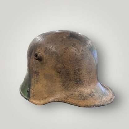 A side view of a German M16 steel camouflage WW1 helmet. The exterior of the helmet has been hand painted in tan ochre, green, and black paint.