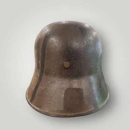 A rear view of a German M16 steel camouflage WW1 helmet. The exterior of the helmet has been hand painted in tan ochre, green, and black paint.