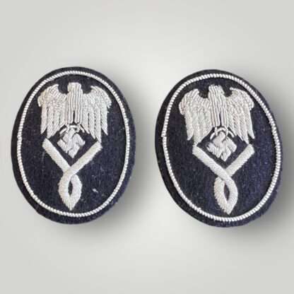 A matching set of Kriegsmarine Intermediate Level Administrative sleeve badges, hand embroidered in silver bullion. The badges despict a Wehrmacht National eagle with down swept wings clutching a canted swastika in its talons, with a single looped chevron below.