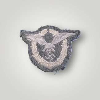 An original Luftwaffe Pilot's Badge in cloth machine embroidered in silver grey thread on blue wool backing. The insignia depicts an oval wreath of laurel and oaks leaves with a flying winged eagle in the centre clutching a canted swastika in its talons.