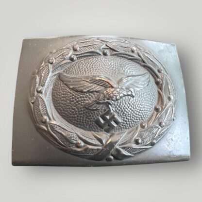 A late war Luftwaffe steel belt buckle, die stamped construction in dark blue steel. The obverse of the buckle the Luftwaffe eagle cluching a canted eagle surrounded laurel wreath with pebbled background.