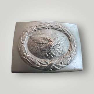 A late war Luftwaffe steel belt buckle, die stamped construction in dark blue steel. The obverse of the buckle the Luftwaffe eagle cluching a canted eagle surrounded laurel wreath with pebbled background.