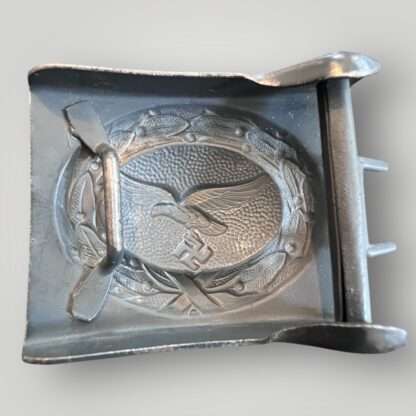 Reverse image of a late war Luftwaffe steel belt buckle, die stamped construction in dark blue steel. The obverse of the buckle the Luftwaffe eagle cluching a canted eagle surrounded laurel wreath with pebbled background.