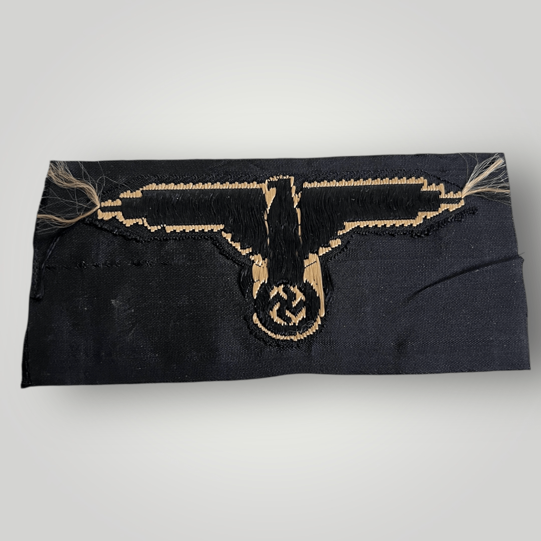 A reverse image of a German Waffen-SS Tropical BeVo Sleeve Badge, flat wire BeVo construction in tan coloured thread on a black background.