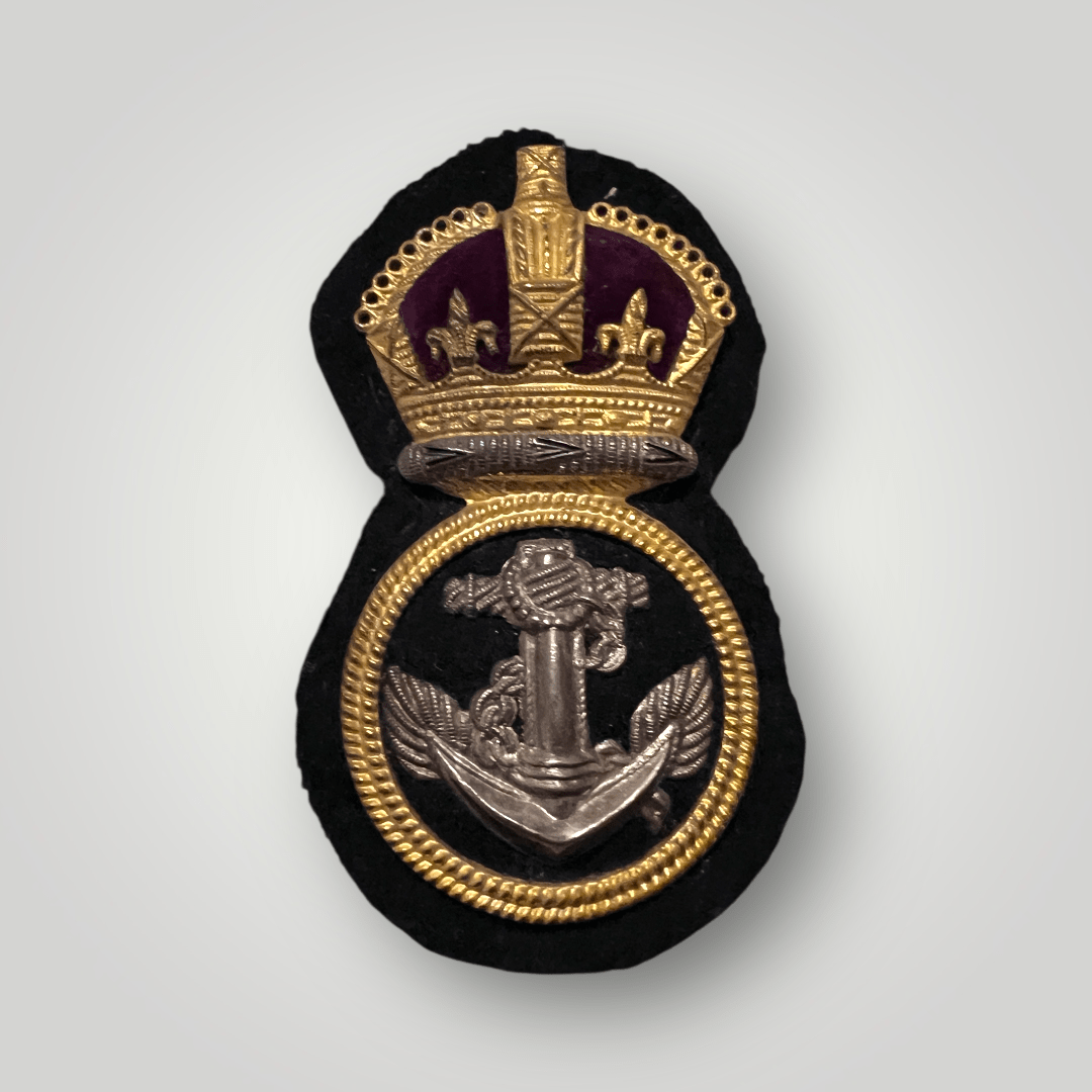 A British WW2 Royal Navy Chief Petty Officers economy cloth badge. The badge depicts a silver anchor, with a wrapped cable, surrounded by a single-ringed gold border within a laurel wreath, surmounted by a King's crown