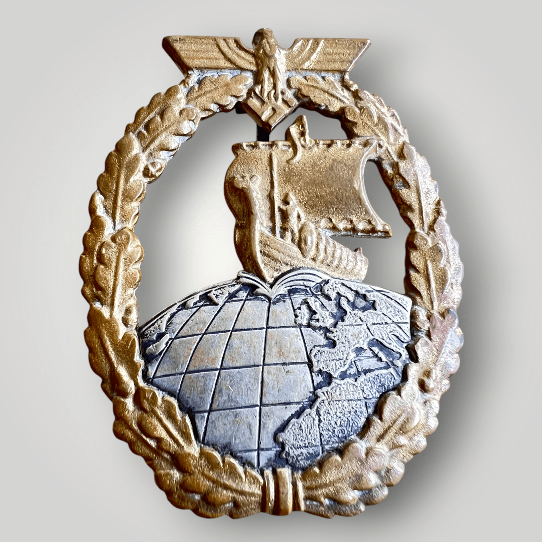 This is an original Kriegsmarine Auxiliary Cruiser Badge by C.E.Juncker. The front features an oval oak leaf wreath with a Kriegsmarine eagle holding a mobile swastika, encircling a central motif of a Viking longship traversing the Northern Hemisphere.
