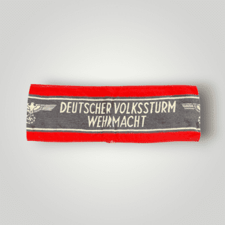 This is an original Deutscher Volkssturm Wehrmacht armband made of screen-printed cotton. It features a central black band with white lettering and Wehrmacht Eagles, bordered by two white lines and red edges.