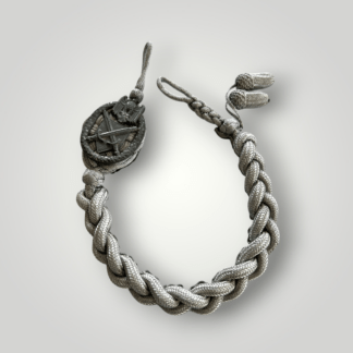 An original German WW2 Heer Infantry Shooting Lanyard, grade 3, and a textbook example. The lanyard is constructed from wire braid, with a die-stamped aluminium emblem depicting an oval oak leaf wreath enclosing a Wehrmacht eagle clutching a swastika above a shield with crossed swords. The end of the lanyard is fitted with two wire-braided acorns, denoting the grade.