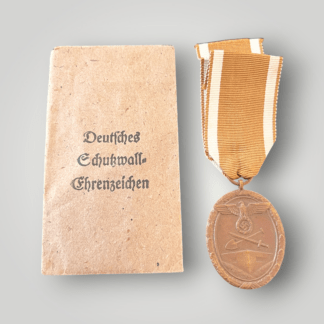 An original West Wall Medal by Carl Poellath, complete with its original presentation packet. The medal is of die-struck alloy construction with a bronze-toned finish and an oval design bordered by overlapping oak leaves.
