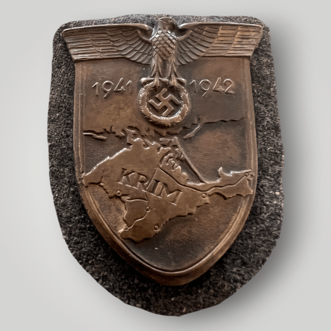 An original Luftwaffe Krim Campaign Shield magnetic version with bronze finish with beautiful patina, mounted on Luftwaffe blue-grey fabric. The reverse of the shield is complete with prongs and papper backing.