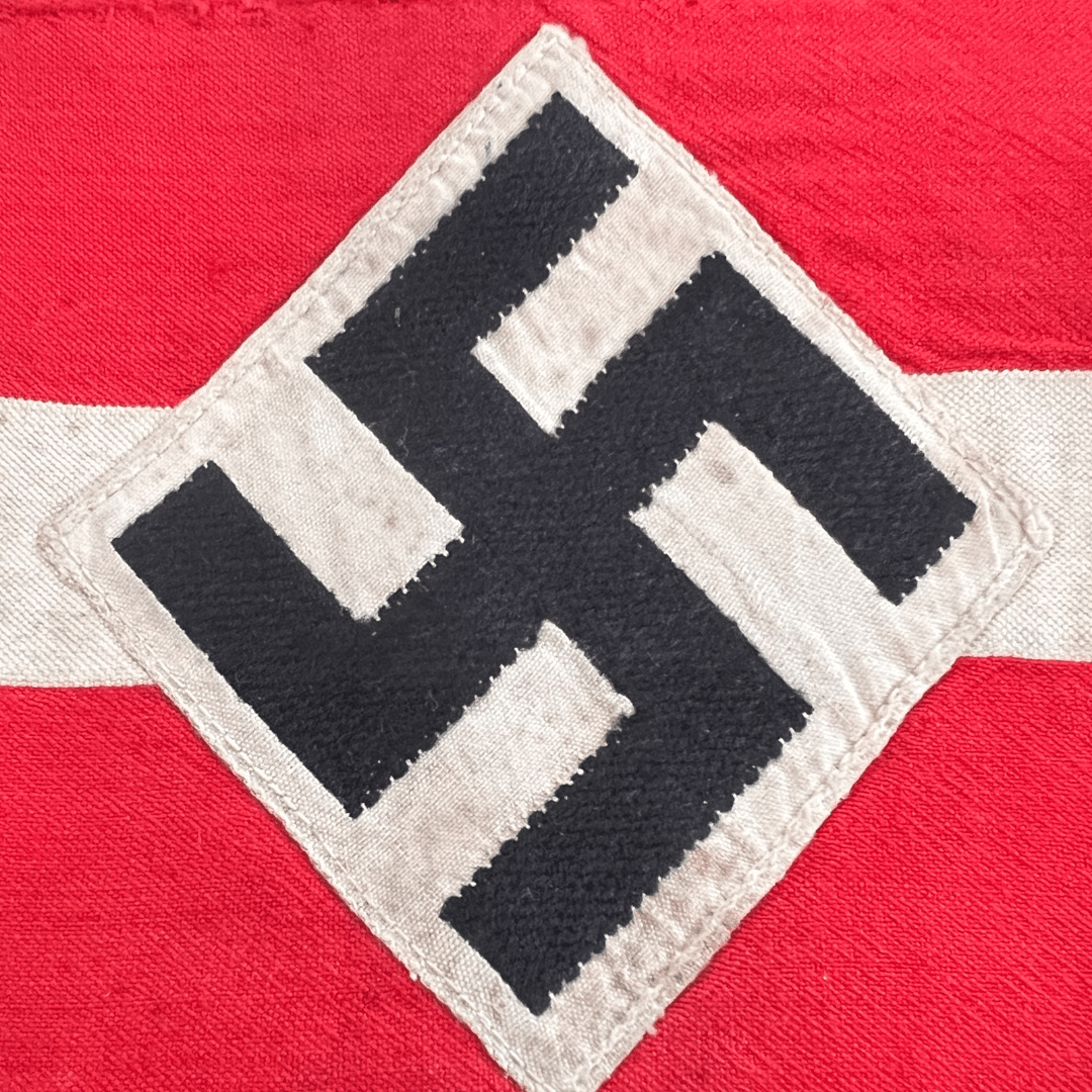 A genuine Hitler Youth cloth armband, constructed in red cotton the exterior bearing a central machine-embroidered white cotton band, overlaid by a white cotton diamond bearing a black mobile swastika.