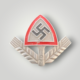 An original RAD National Labour Corp Cap Badge (Reichsarbeitsdienst), constructed in aluminium. The badge features a black mobile swastika set upon an upturned spade that is edged in red.