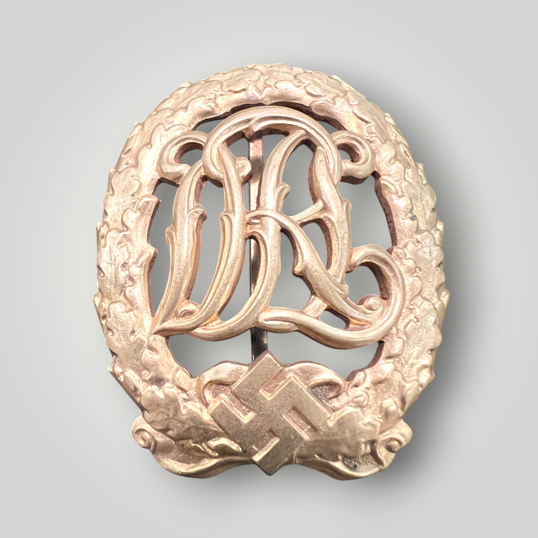 An original German DRL Sports Badge Gold, tombac construction. The obverse consists of "DRL' script superimposed in the centre surrounded by an oak wreath with a swastika and bow below.