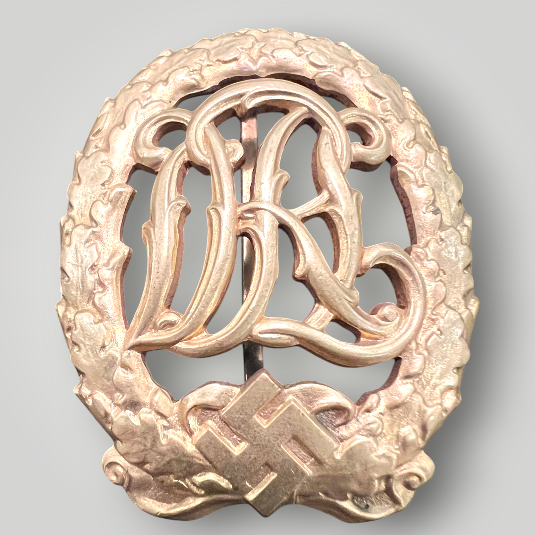 An original German DRL Sports Badge Gold, tombac construction. The obverse consists of "DRL' script superimposed in the centre surrounded by an oak wreath with a swastika and bow below.