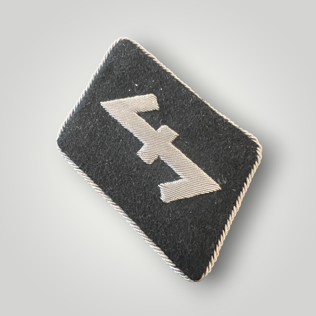 A scarce Waffen-SS 23rd SS Nederland Division officer’s collar tab. The collar tab is hand-embroidered in silver bullion on black doeskin material with silver twisted braid around the edges. The collar tab features a ‘Wolfsangel’ symbol which was believed to ward of wolves in ancient times.