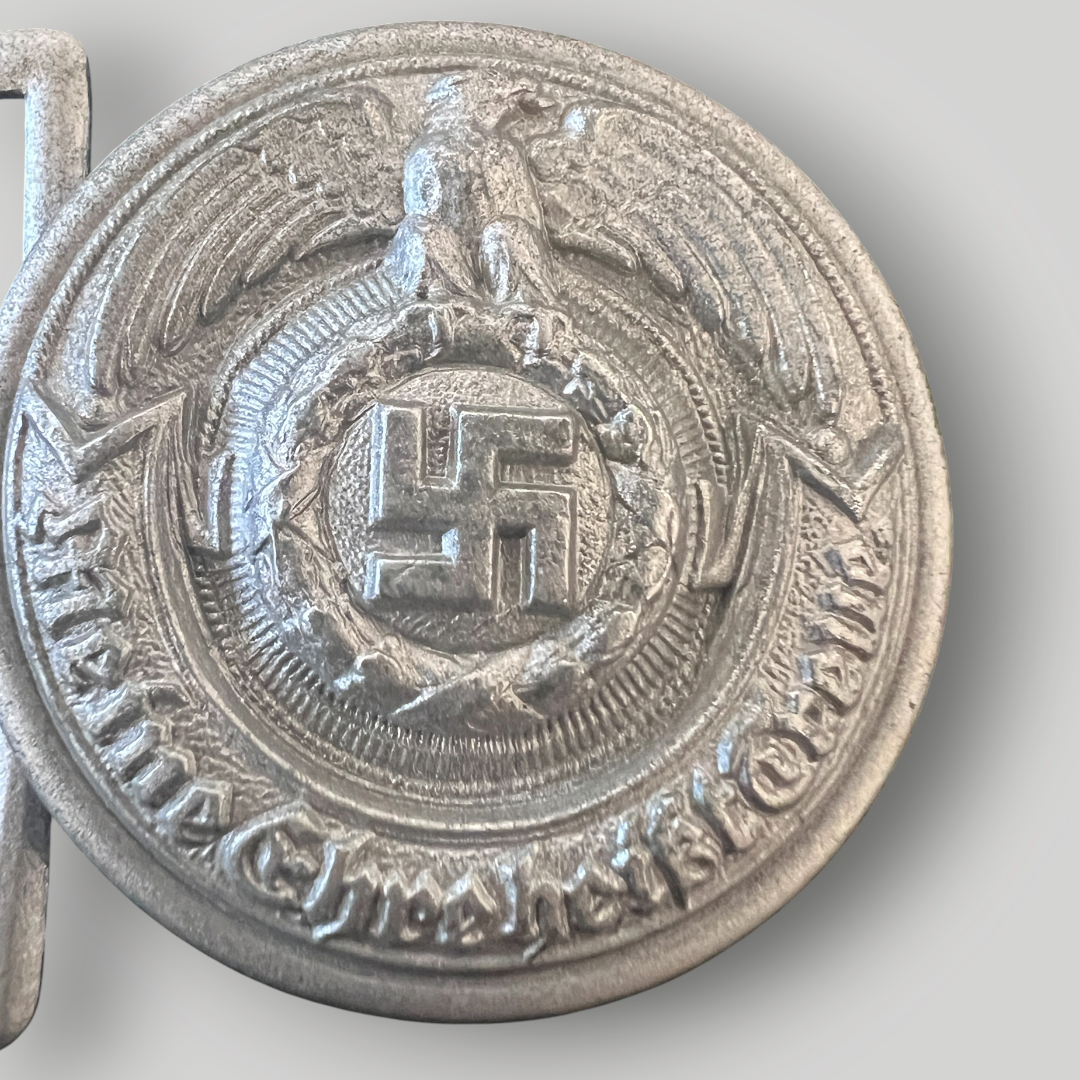 An original Waffen-SS Officer’s Belt Buckle Stamped SS RZM 36/42 OLC, constructed in a zinc. The obverse of the SS officer's belt buckle is round and depicts an eagle with outstretched wings clutching a wreathed swastika in its talons, with a scroll below with the inscription 'Meine Ehre heißt Treue’ (My Honour Is Loyalty).