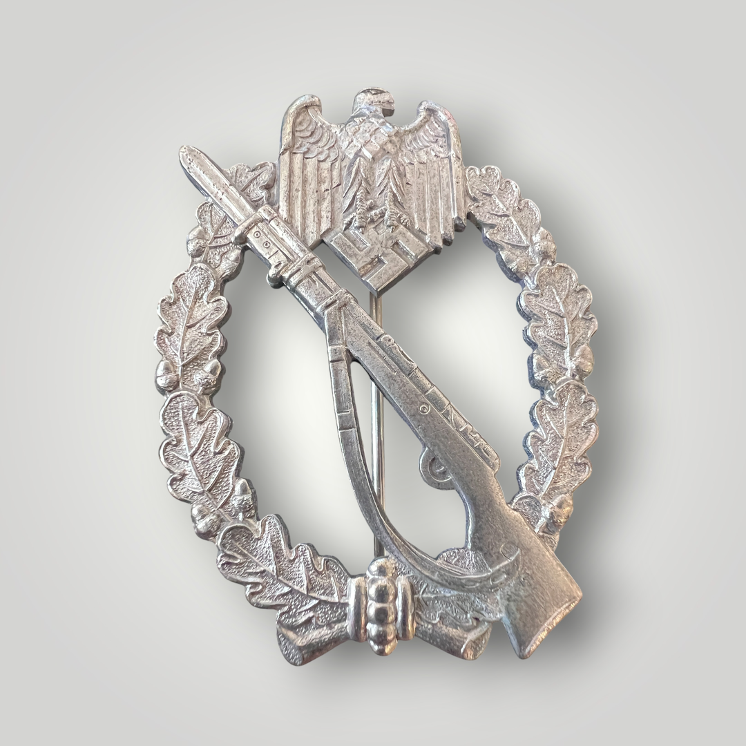 An original German WW2 Infantry Assault Badge by Paul Meybauer, constructed from silver-plated zinc. The obverse features an oval oak-leaf wreath with a diagonally K98 rifle with fixed bayonet and sling, surmounted by a Wehrmacht eagle clutching a canted swastika.
