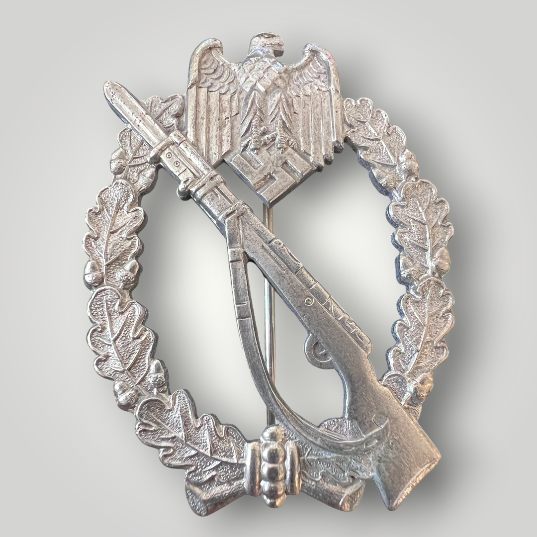 An original German WW2 Infantry Assault Badge by Paul Meybauer, constructed from silver-plated zinc. The obverse features an oval oak-leaf wreath with a diagonally K98 rifle with fixed bayonet and sling, surmounted by a Wehrmacht eagle clutching a canted swastika.